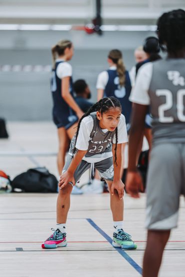 Young basketball player in gray jersey catching her breath during a game.
