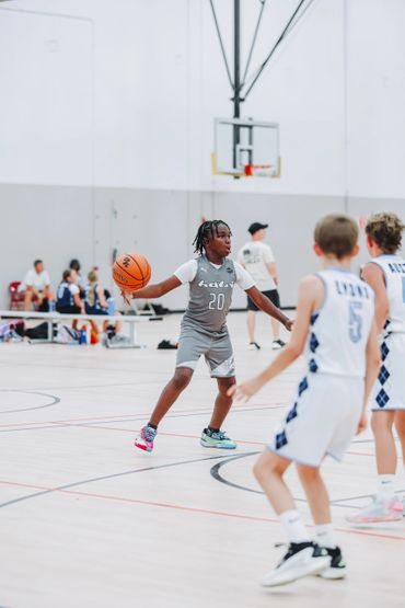 Young basketball player in gray jersey dribbling past opponents on indoor court.