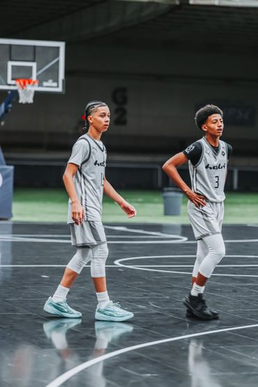 Two young basketball players in grey uniforms on an indoor court.