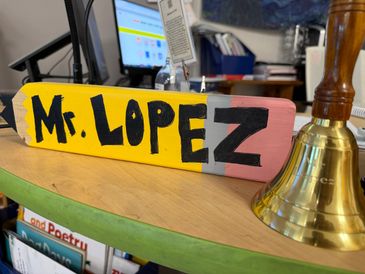 A colorful desk nameplate reading 'Mr. Lopez' with a brass bell beside it.