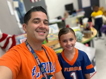 A man and girl wearing Florida Gators shirts smile in a classroom.