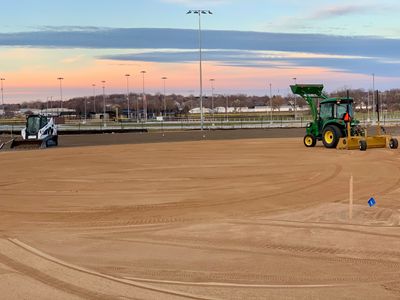 Construction vehicles preparing a large dirt field at sunset.