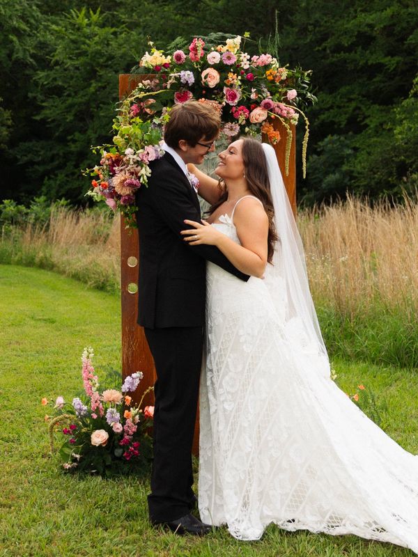 Bride and groom embracing outdoors with floral arch.