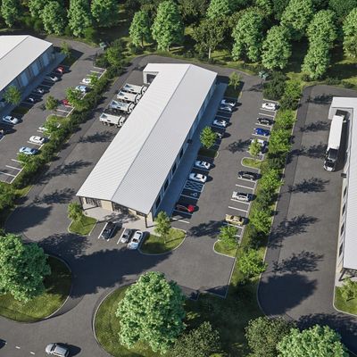 Aerial view of a modern warehouse surrounded by trees and parked vehicles.