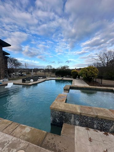 A serene backyard pool with clear water under a partly cloudy sky.