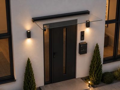 Modern black front door with glass canopy and warm lighting on a white wall.