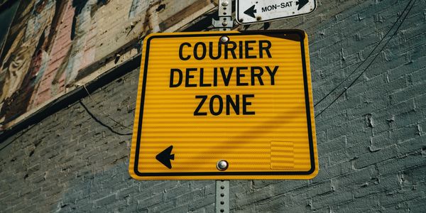 Yellow sign indicating a courier delivery zone with an arrow pointing left.