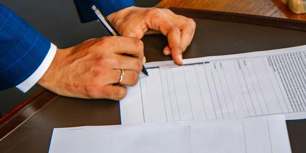 Person in blue suit signing a document on a desk.
