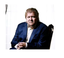 Man in a blue suit sitting on a chair with serious expression.