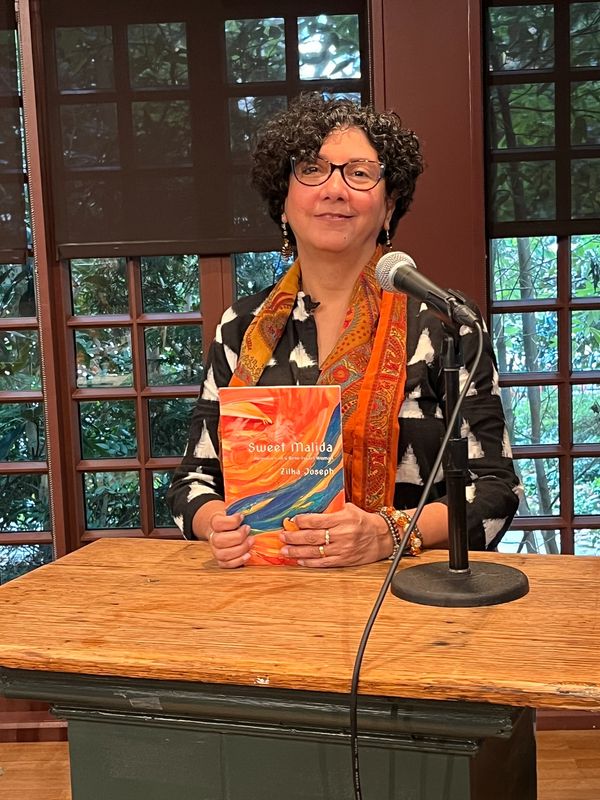 Woman holding a book titled 'Sweet Malida' at a microphone.