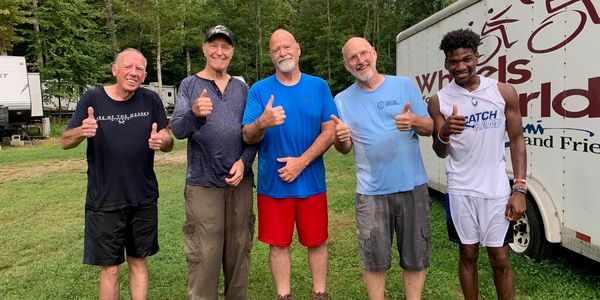 Five men standing outdoors giving thumbs up.