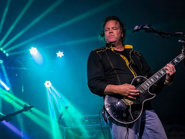 Guitarist passionately playing on stage with vibrant blue and green lights.