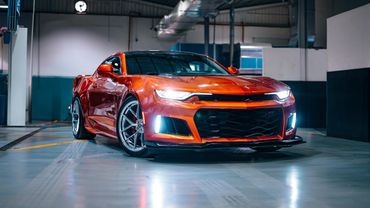 Shiny orange sports car with headlights on in a garage.