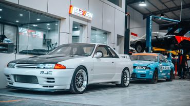Two modified cars inside a garage with one on a lift.