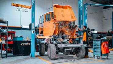 Mechanic working on an orange vehicle chassis in a modern maintenance garage.