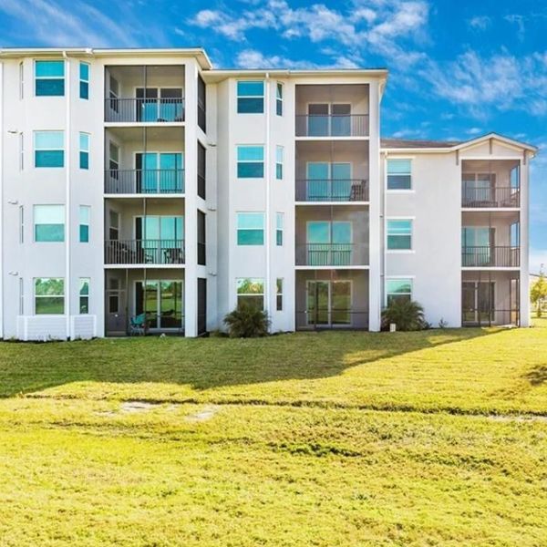 Modern white apartment building with balconies under a bright blue sky.