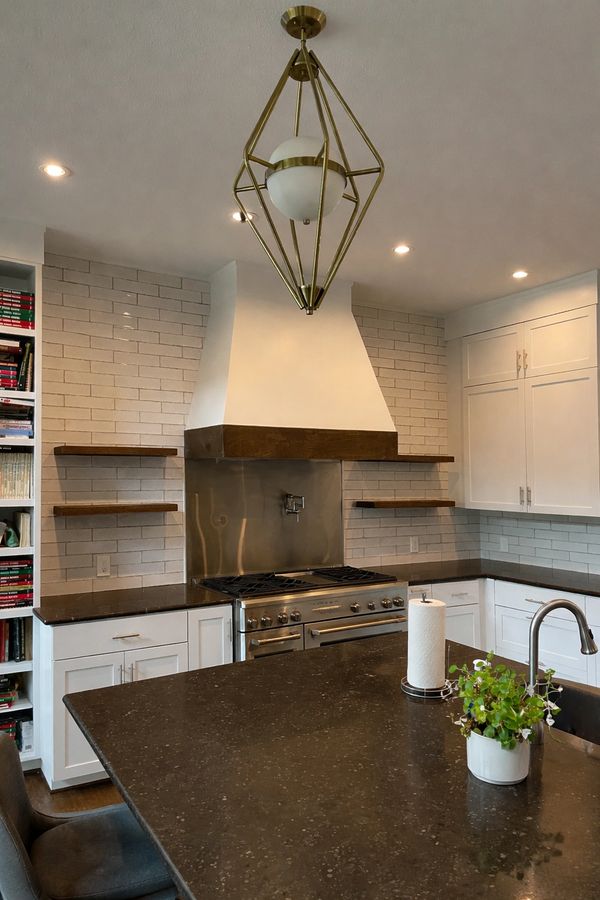 Modern kitchen with white cabinets, dark countertops, and a geometric brass light fixture.