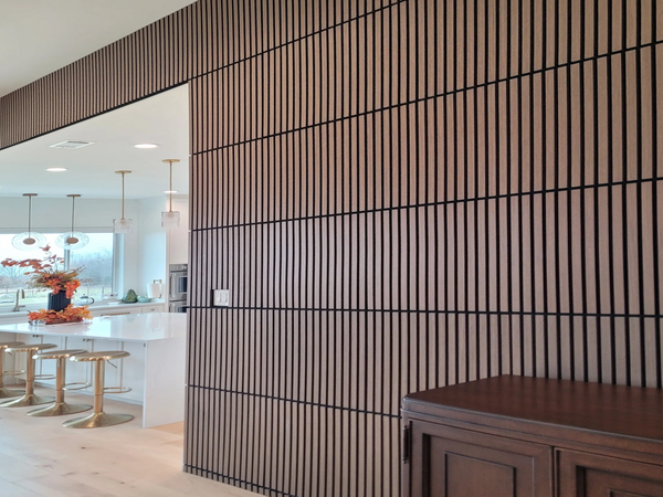 Modern kitchen with a white island and gold stools beside a wood-paneled wall.