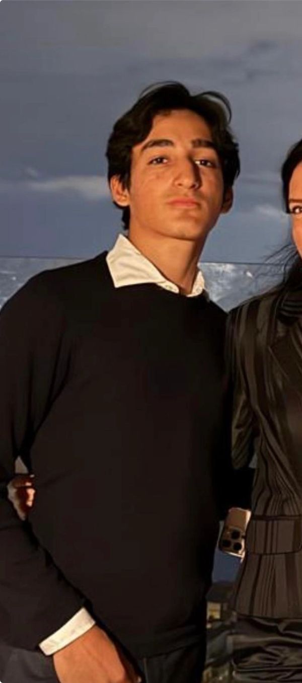 Young man in a black sweater and white collar posing outdoors.