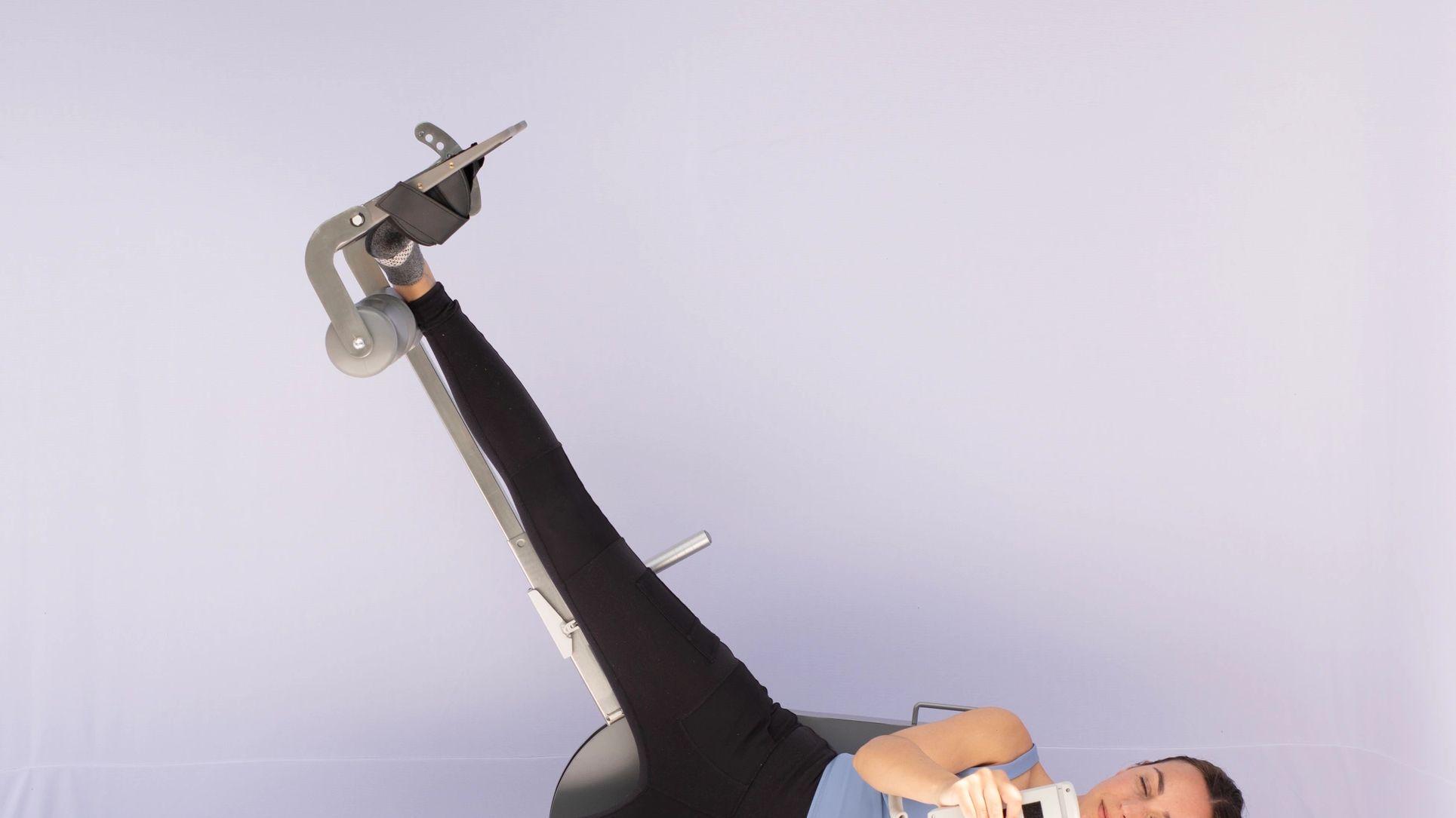 Woman using leg exercise equipment while lying on her side and holding a remote.