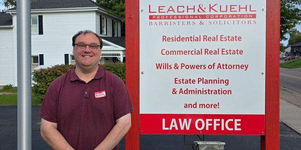 Man in burgundy shirt stands beside a law office sign.