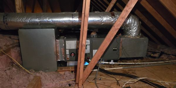 HVAC unit installed in an attic with ductwork and wooden beams.