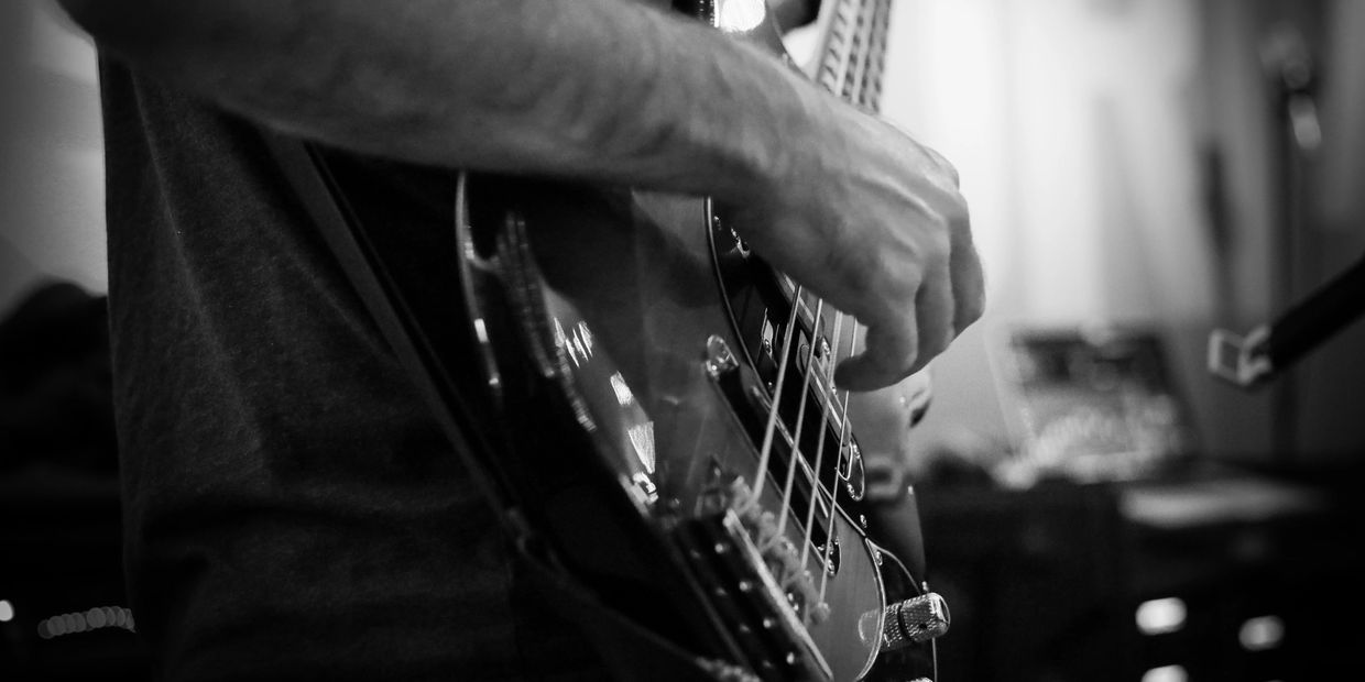 Close-up of a person playing an electric bass guitar in black and white.