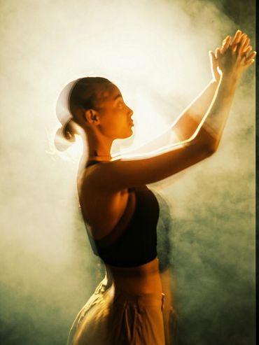 Woman in motion with hands raised, illuminated by soft golden light.
