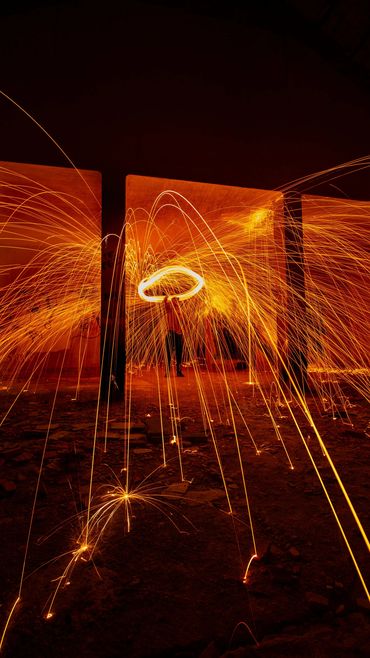 Person spinning steel wool, creating bright sparks in a dark setting.
