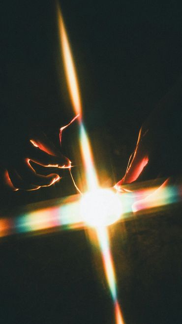 Hands gently holding a glowing light with colorful rays in the dark.