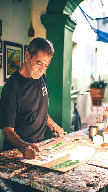 An elderly man painting a detailed artwork on a rustic table.