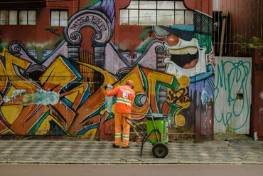A sanitation worker cleans the street in front of colorful graffiti.