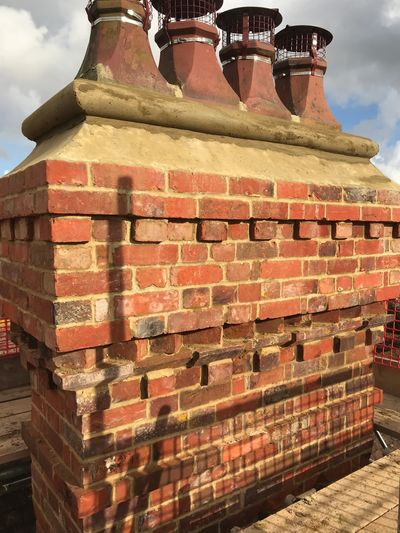A detailed brick chimney with four metal-capped flues under a partly cloudy sky.