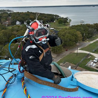 Diver in a red helmet gives a thumbs-up from a blue platform with a lake in the background.