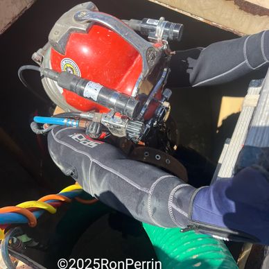 Diver in wetsuit preparing to enter water with equipment and helmet.