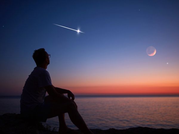 Silhouette of a man looking at the Moon and stars over sea ocean horizon