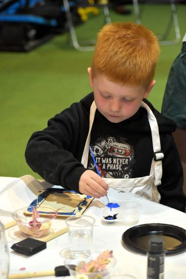 Young boy focused on painting with blue paint at a table.