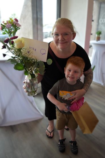 Smiling woman and boy holding flowers and gift bag indoors.