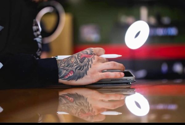 Tattooed hand holding a stylus over a tablet.