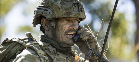 Soldier in camouflage gear and helmet with communication radio up to mouth and ear.