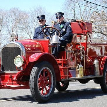 Antique Fire Engine with one fireman driving and one sitting in the passenger seat dressed in old ti