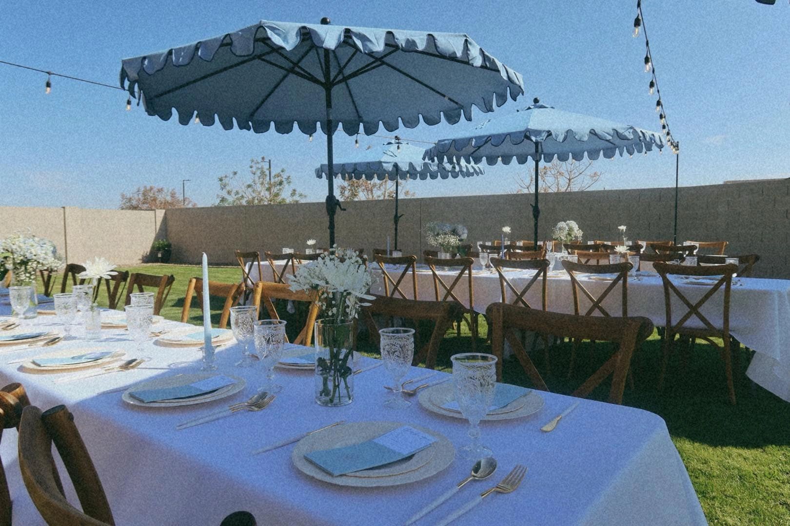 Elegant outdoor dining setup with blue umbrellas and white tablecloths.