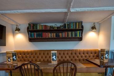 Cozy pub seating with wooden chairs, tufted leather bench, and a bookshelf above.
