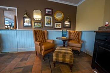 Cozy corner with vintage chairs, a plaid ottoman, and framed mirrors on the wall.