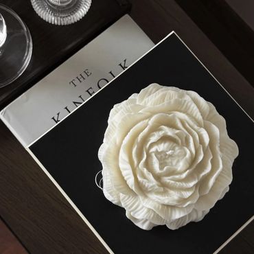 A white flower-shaped candle on a black book with a magazine underneath.