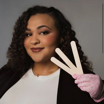 Smiling woman with curly hair holding wooden tongue depressors wearing a pink glove.