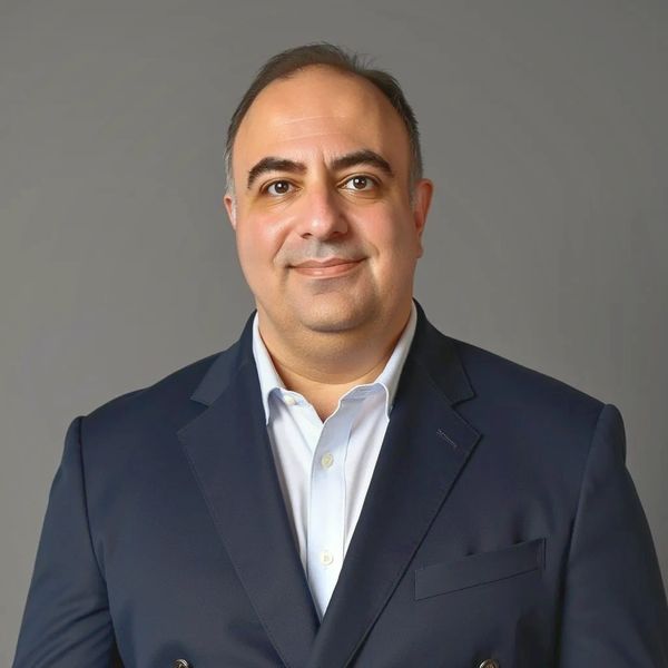 Smiling man in a navy blazer and white shirt against a gray background.