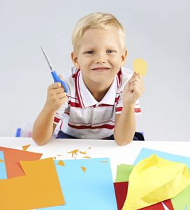 Smiling boy with scissors and paper crafts.