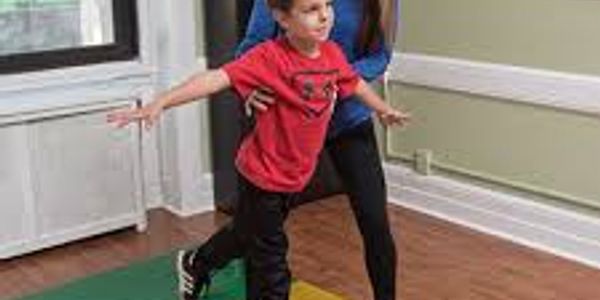 Adult assists child in balancing exercise indoors.