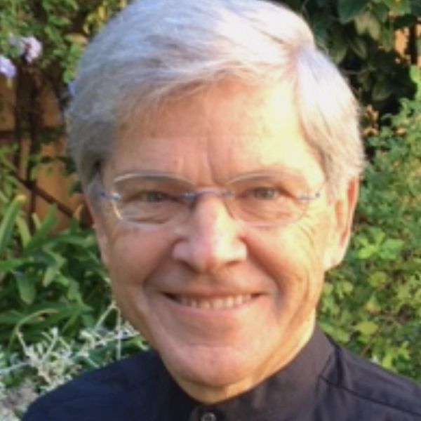 Smiling elderly man with gray hair and glasses in a garden.